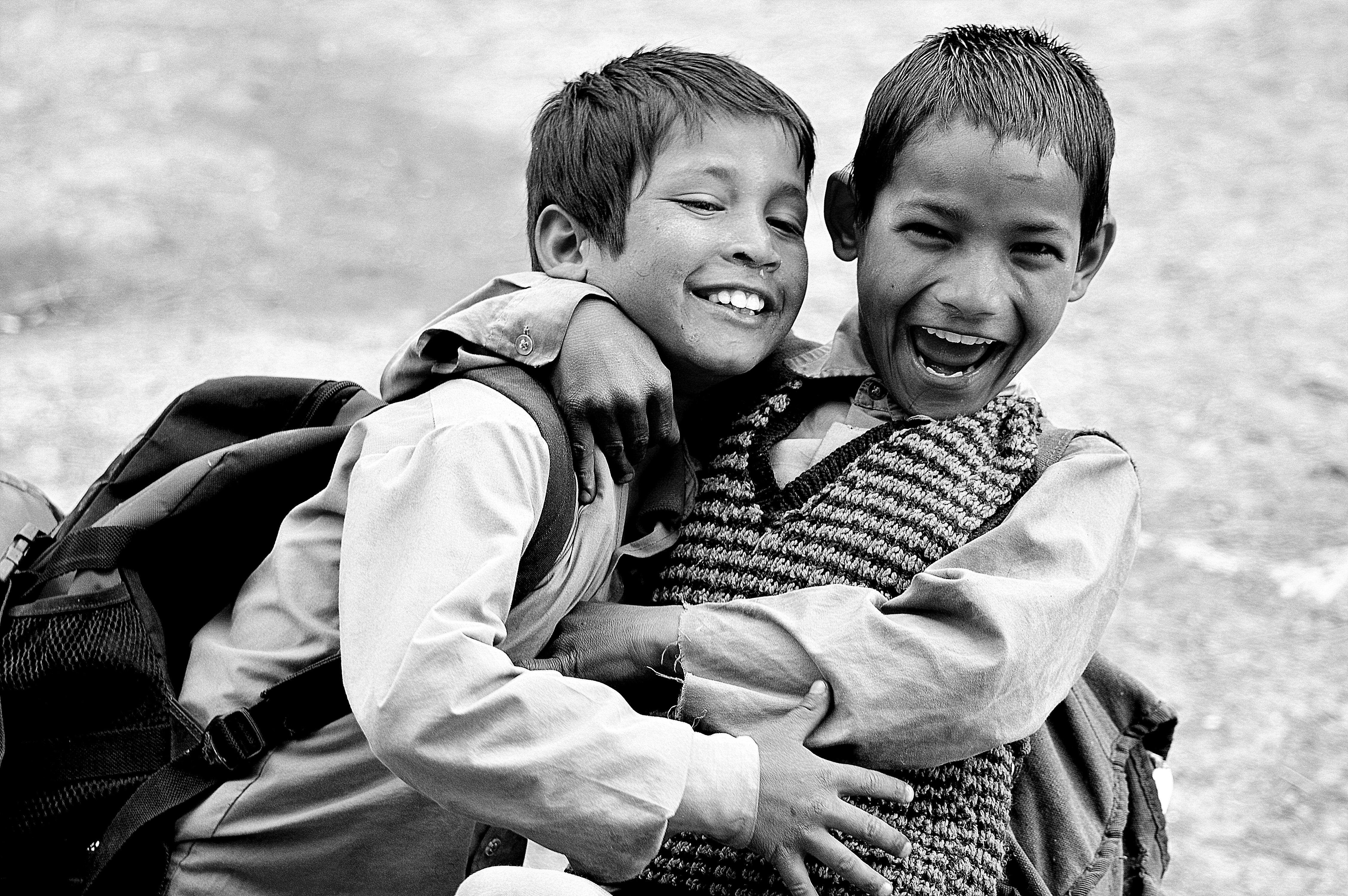 grayscale photography of two boys hugging while laughing